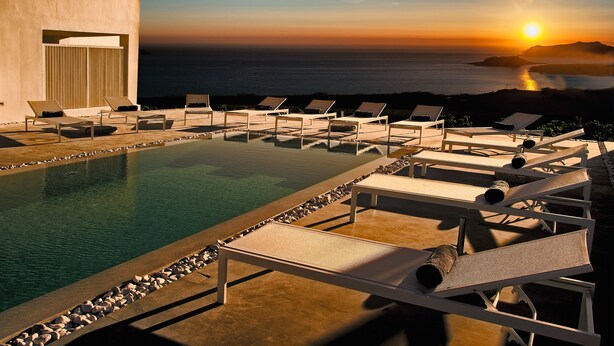 A poolside area with lounge chairs and a view of the sunset over the ocean. - May Seven Santorini (Santorini)