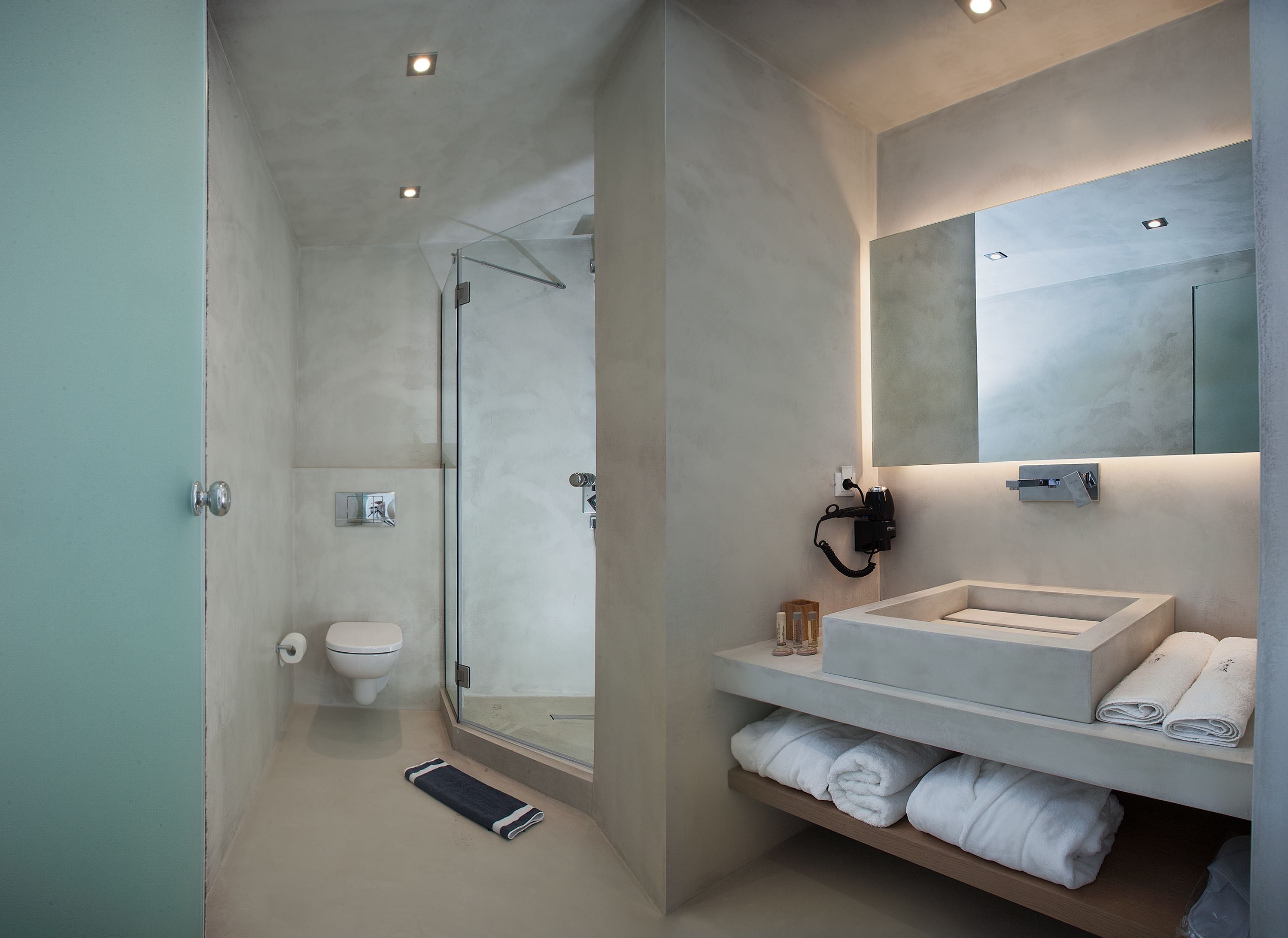 A modern bathroom with a glass shower enclosure, a toilet, a vanity with a mirror, and neatly folded towels.