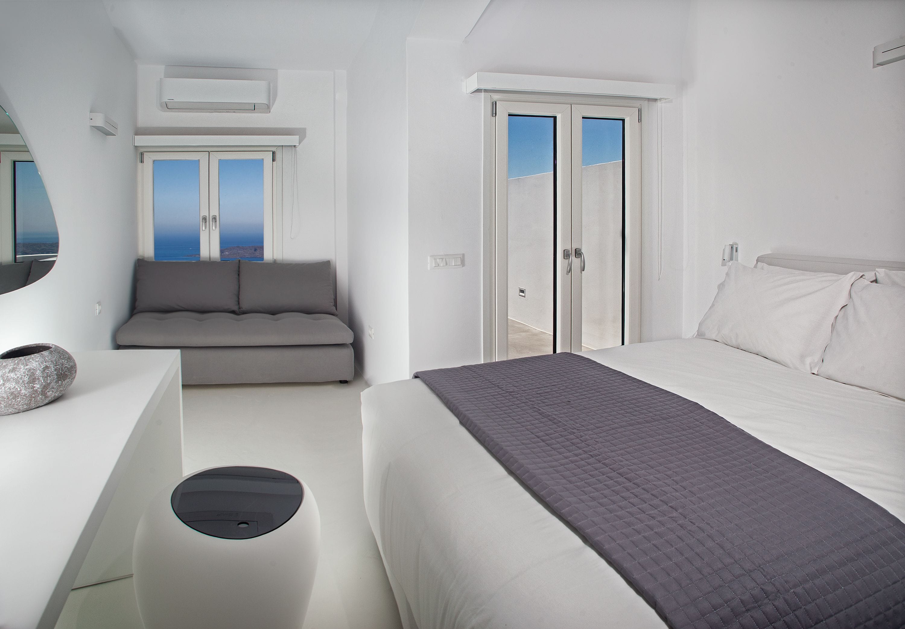 A modern bedroom with a bed, a sofa, and a view of the sea through a door.