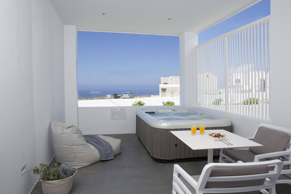 A balcony with a hot tub, seating, and a table with drinks.