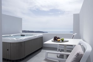 A balcony with a hot tub, a table with fruits, and a view of the sea. - May Seven Santorini (Santorini)