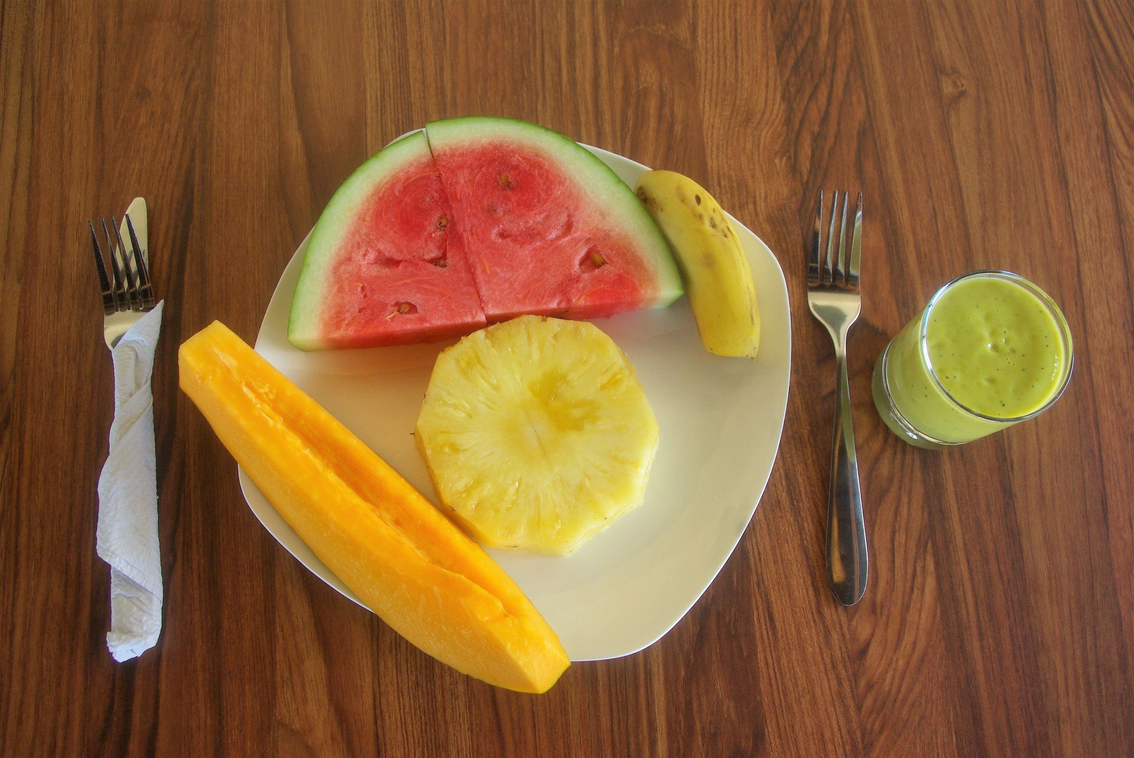 Une assiette contenant une tranche de pastèque, un ananas et une mangue, posée sur une table en bois.