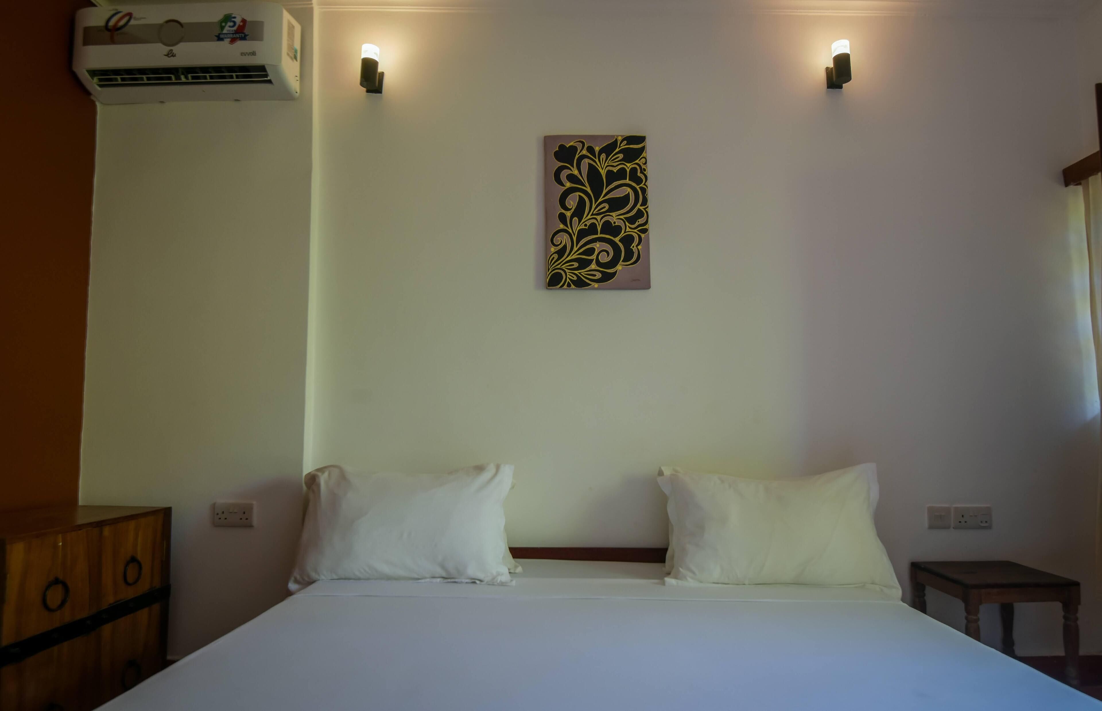 Une chambre à coucher comprenant un lit, deux oreillers, un climatiseur fixé au mur et deux lampes fixées au mur.