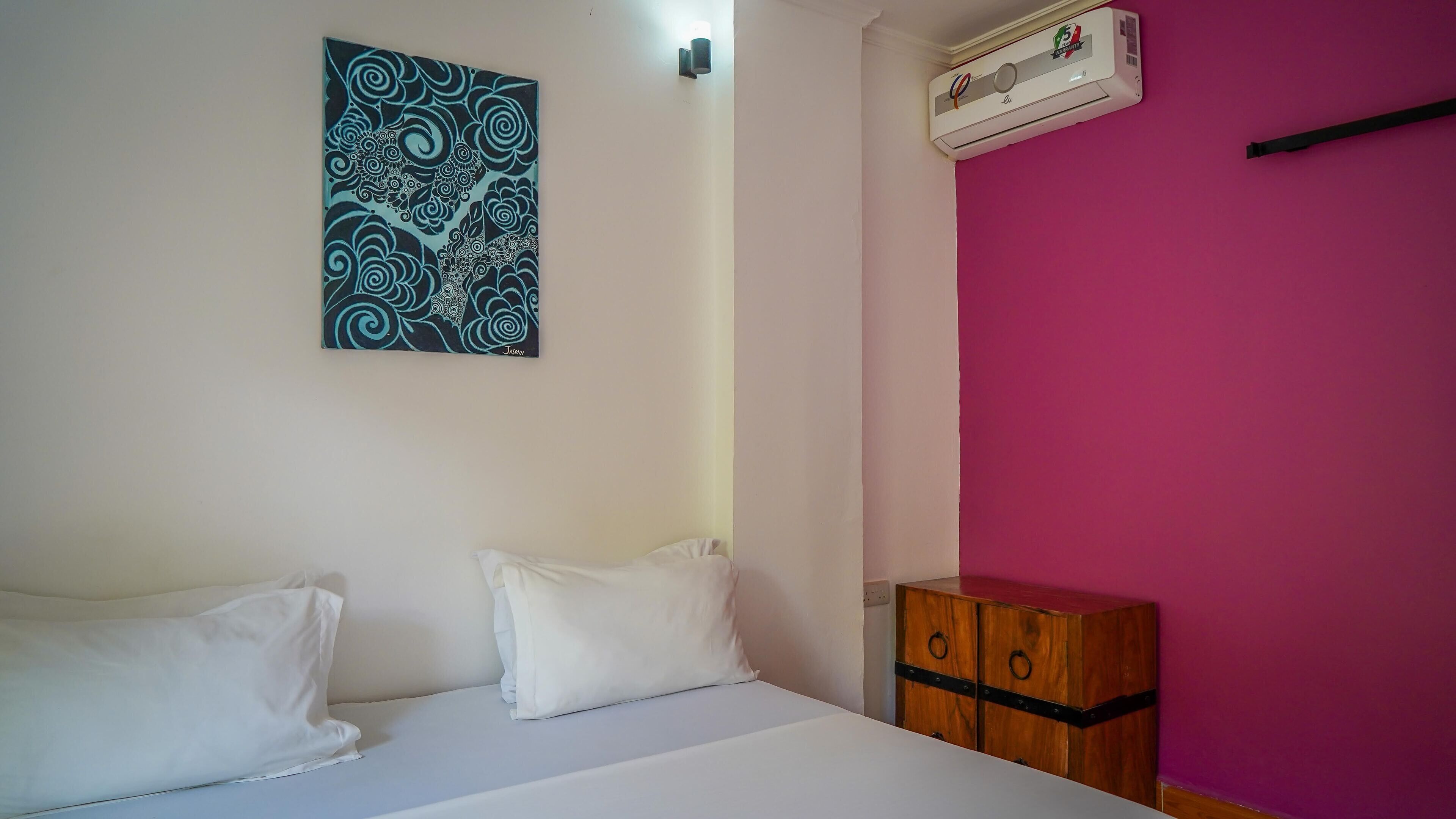 A room with a bed, two pillows, a wall-mounted air conditioner, and a wooden chest of drawers.