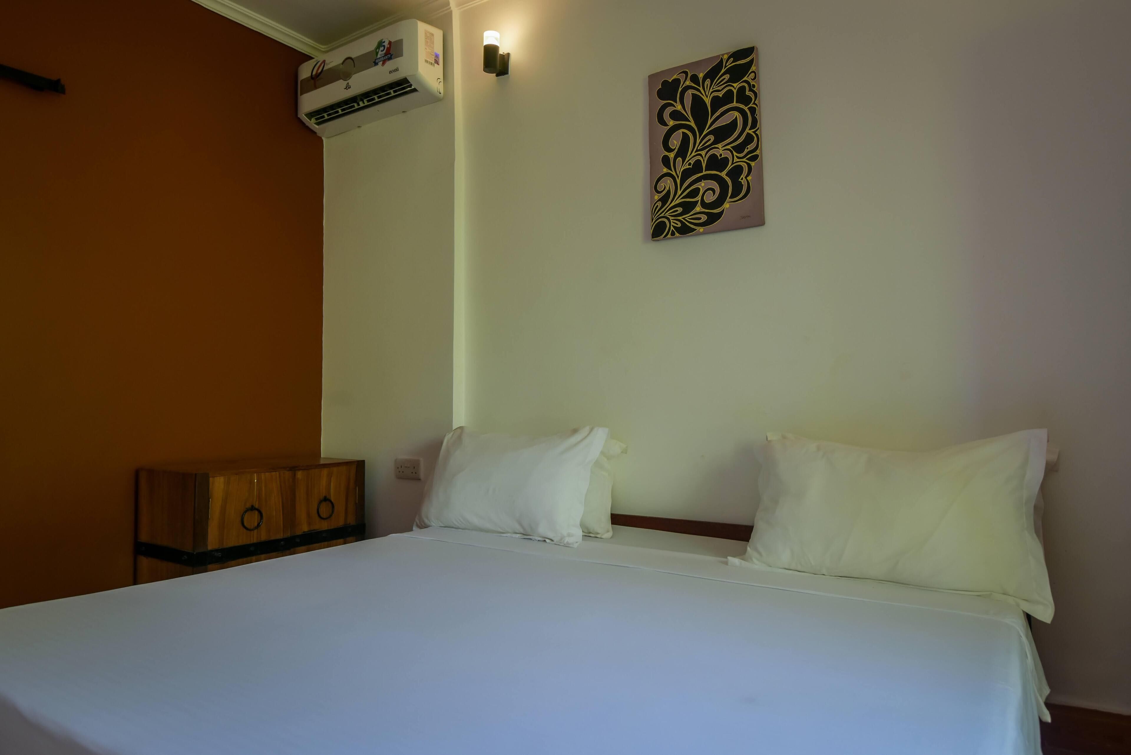 Une chambre d’hôtel comprenant un lit, une commode en bois, un appareil de climatisation et un luminaire fixé au mur.