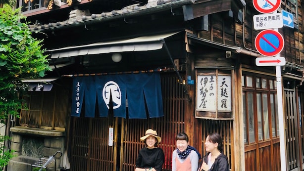 A traditional Japanese building with a sign indicating a restaurant. There are three people sitting outside on a bench. - Kangaroo Hotel (Tokyo)
