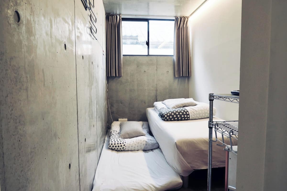 Une petite pièce compacte avec deux lits superposés, une fenêtre avec des rideaux et un mur en béton.