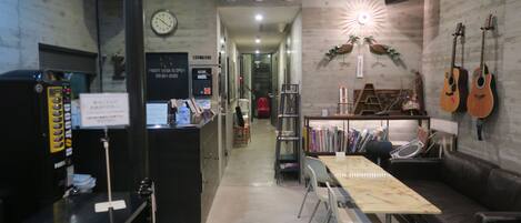 A modern interior with a reception desk, a coffee machine, a clock, a bookshelf, and guitars on the wall.