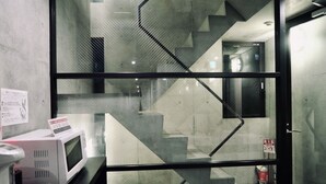 A modern interior with a glass partition, a microwave on a counter, and a staircase leading to another area. - Kangaroo Hotel (Tokyo)