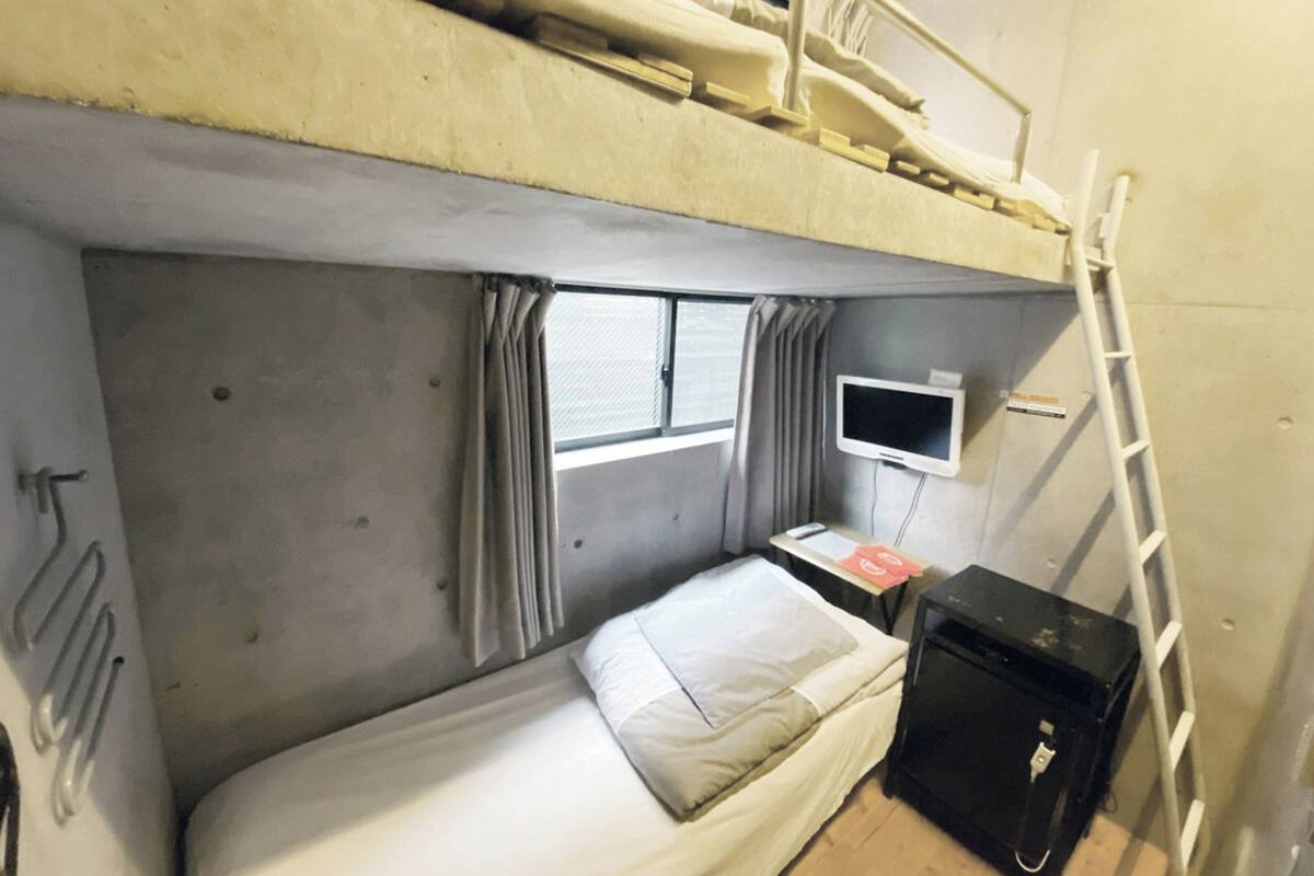 Une chambre avec un lit superposé, une télévision, une petite table et une valise.