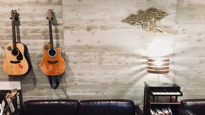 A room with a marble floor, two guitars on the wall, a black leather couch, a bookshelf with magazines, and a piano. - Kangaroo Hotel (Tokyo)