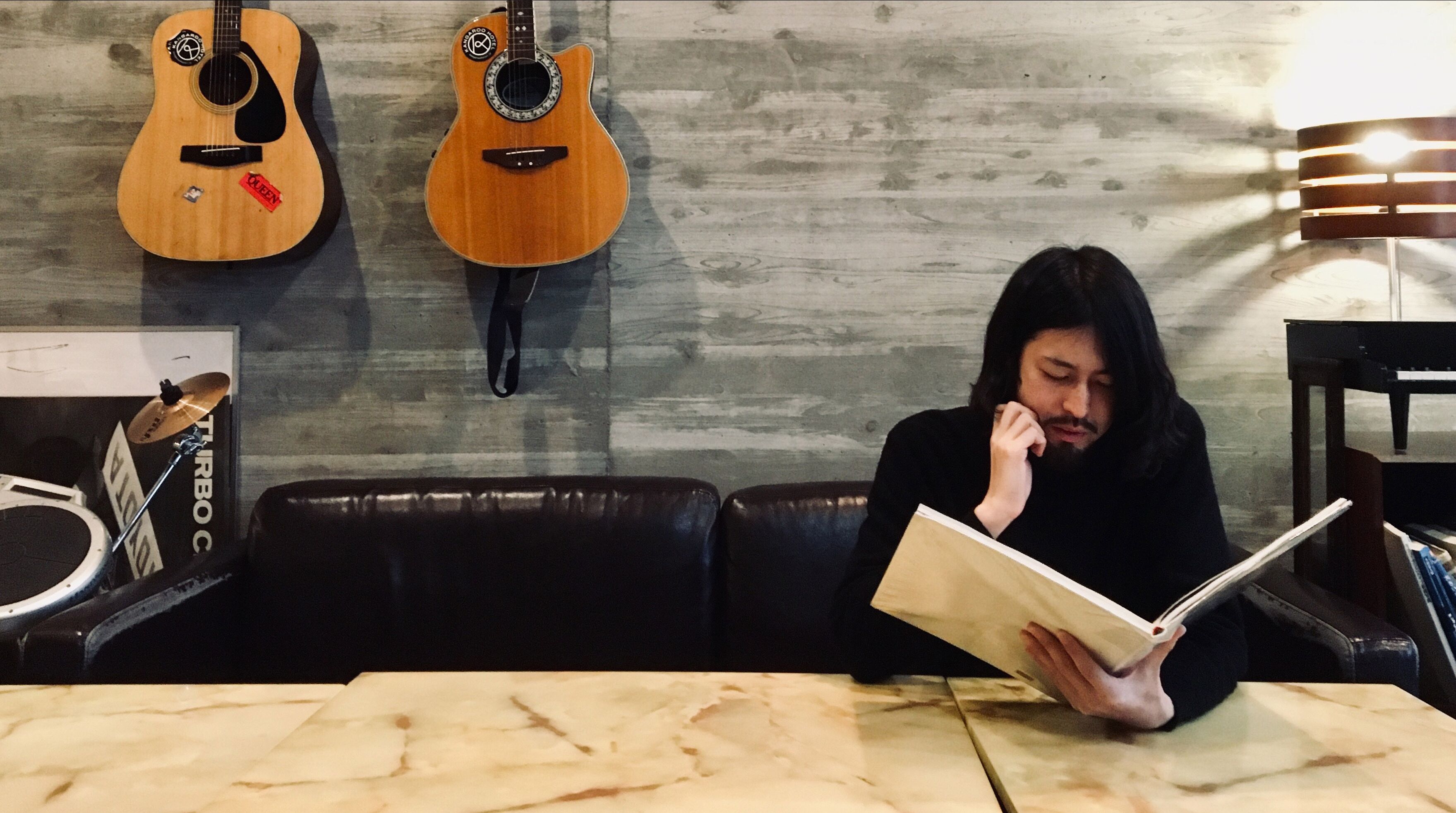 A person reading a book in a room with two guitars on the wall.