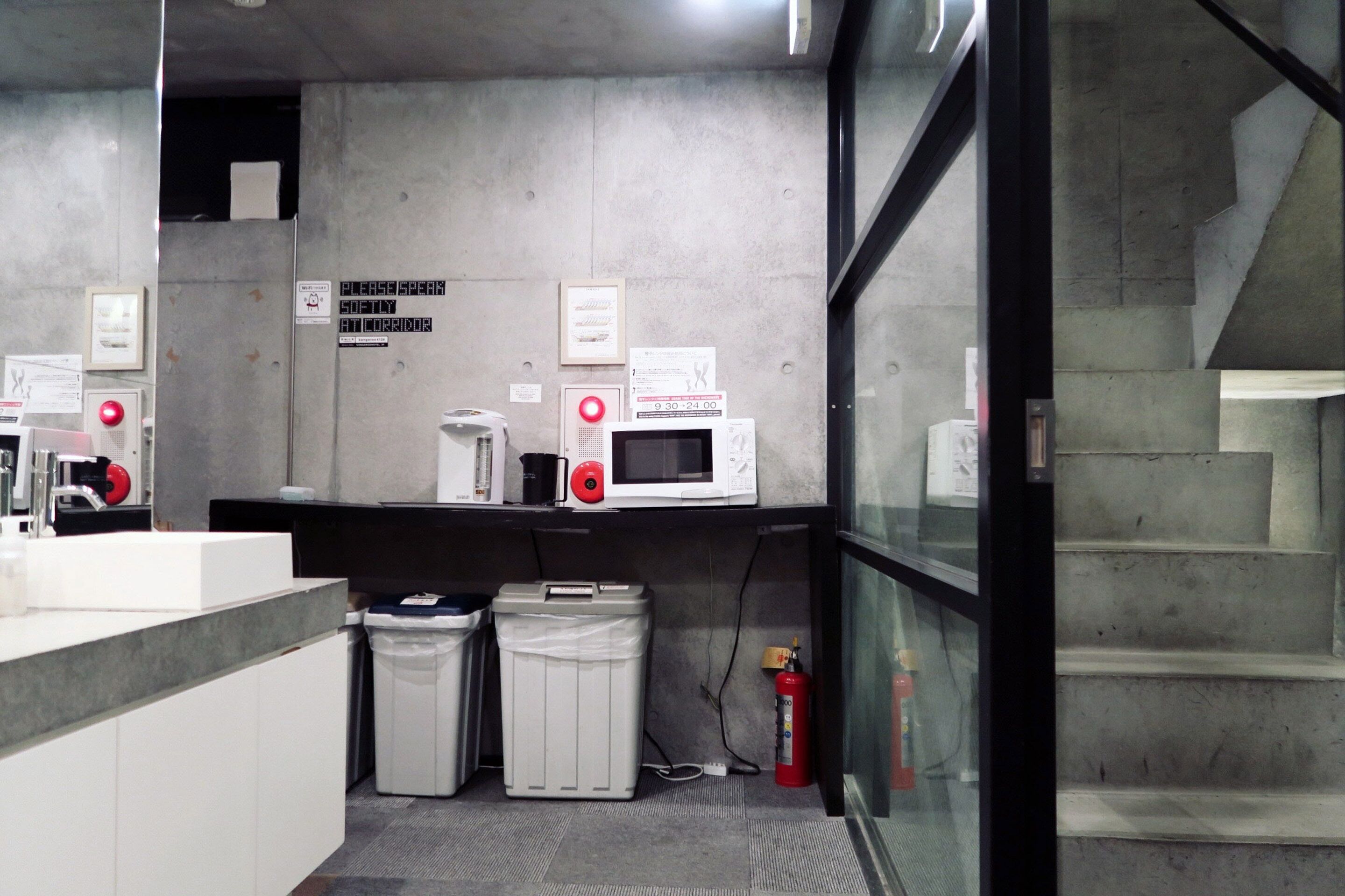 A modern kitchen with a microwave, coffee maker, and a trash bin. There is a fire extinguisher and a staircase visible.