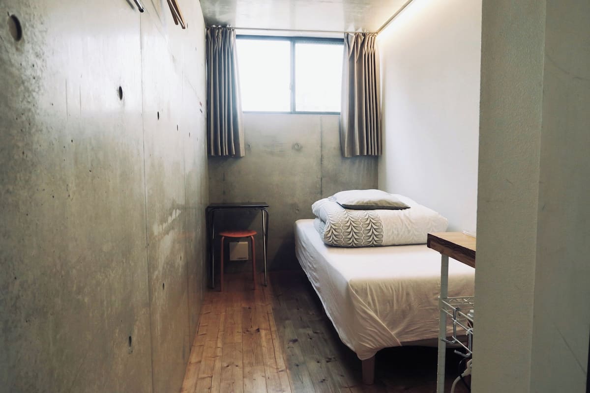 Une petite pièce étroite, avec un lit simple, une petite table et une chaise.