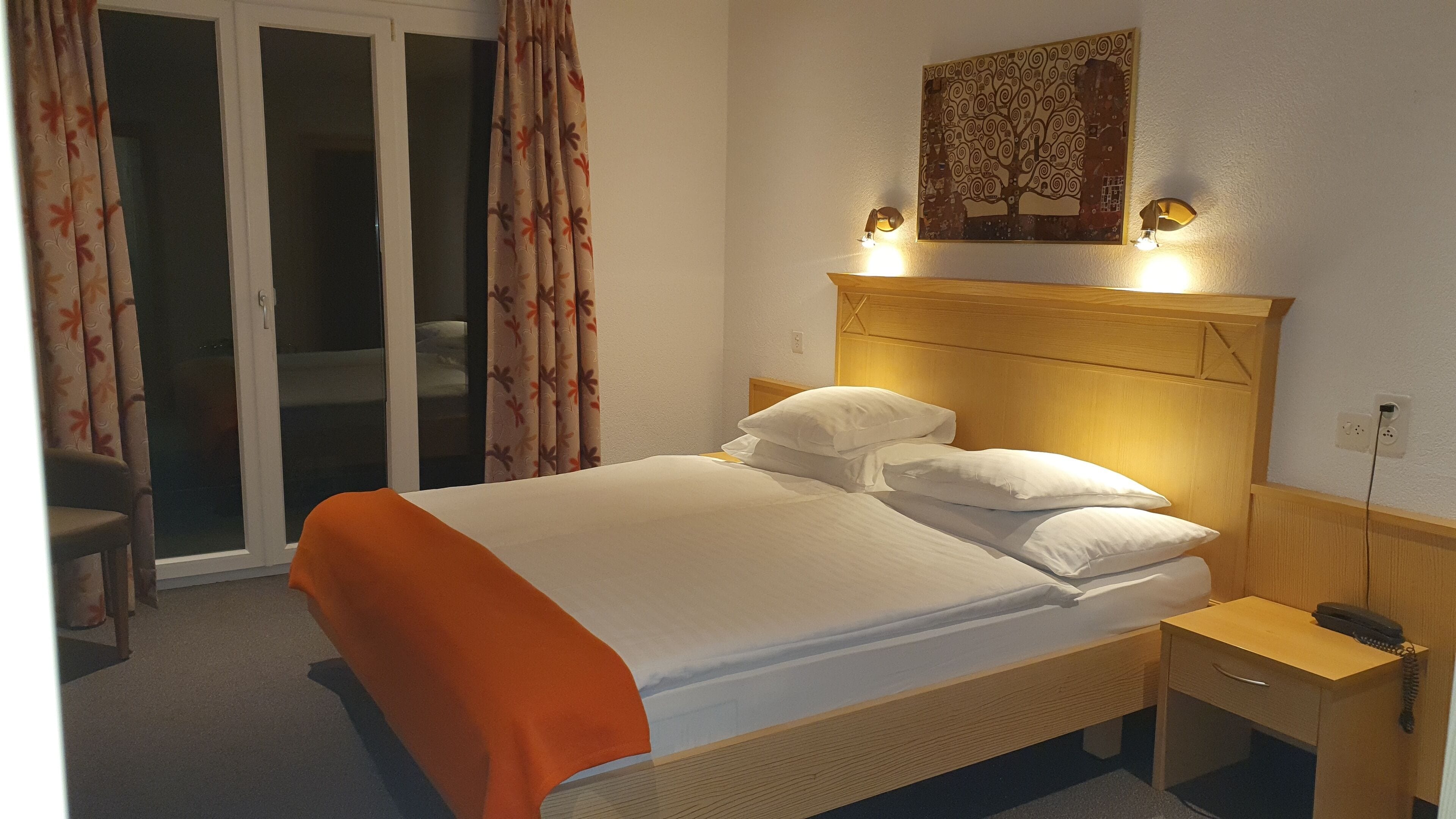 A hotel room with a bed, a nightstand, a telephone, and a painting on the wall.