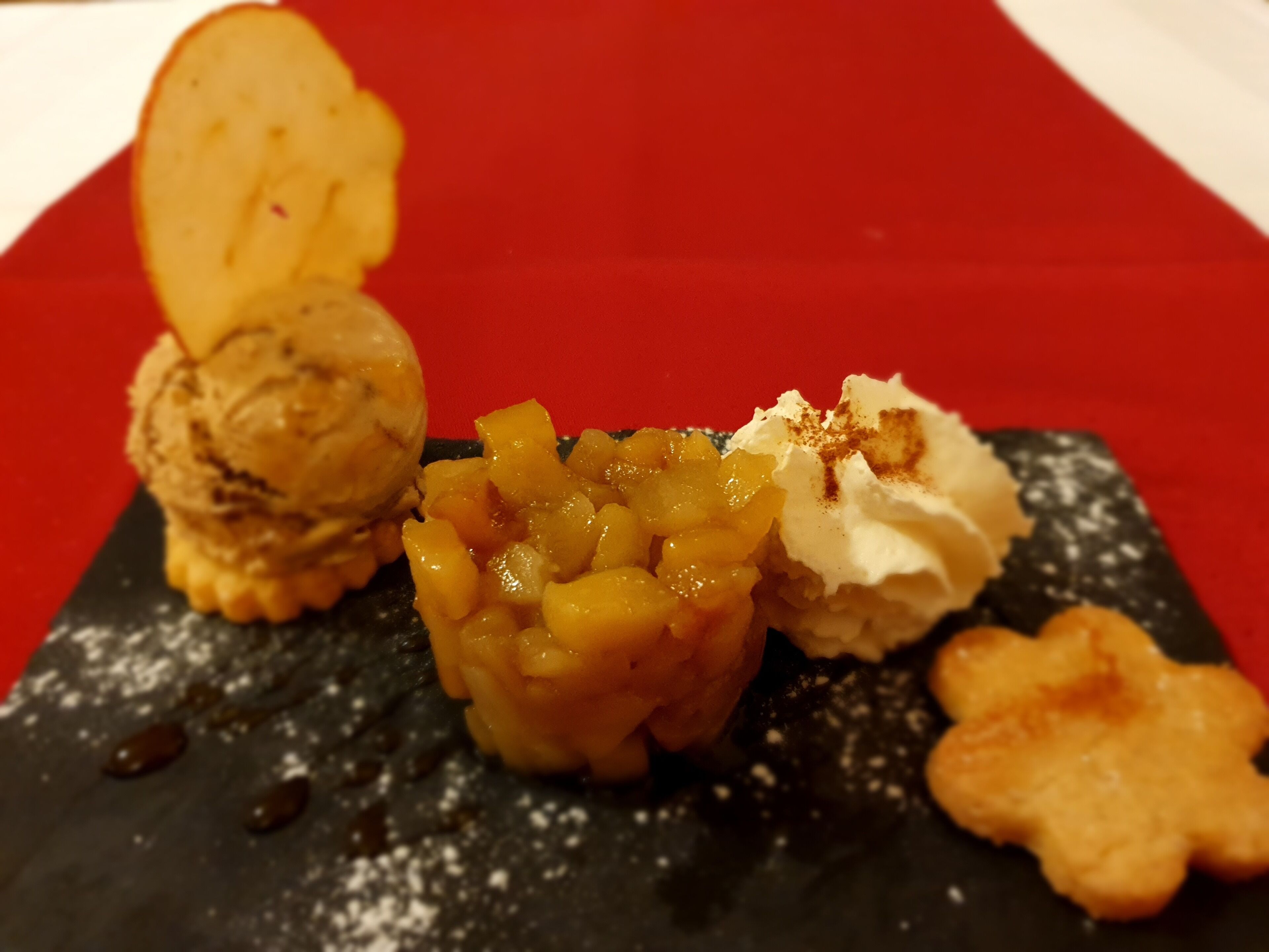 A dessert plate with various items including a scoop of ice cream, a fruit compote, whipped cream, and a cookie.