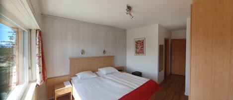 Un dormitorio con una cama de madera, una mesita de noche, una ventana con cortinas, una lámpara de pared y una puerta.