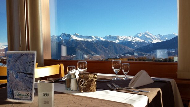 A table set for dining with a mountain view, a menu, and a bottle of water. - Hôtel Splendide (Crans-Montana)