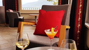 A hotel room with a view of mountains, a red pillow on a chair, and two glasses of wine on the table. - Hôtel Splendide (Crans-Montana)