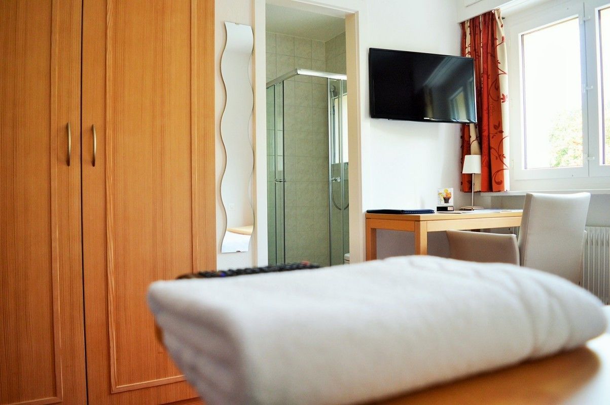 A hotel room with a bed, a desk, a TV, and a shower area.