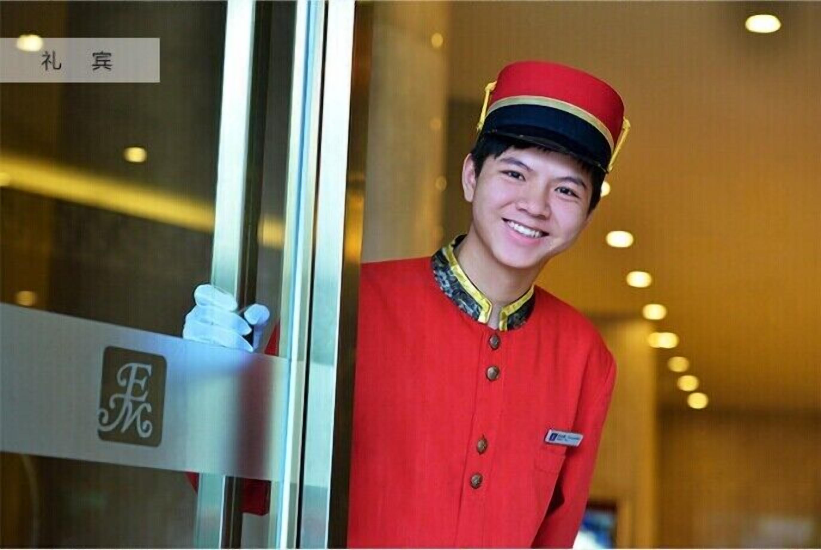 A person in a red uniform with a name tag, standing in a doorway with a sign that reads "F".
