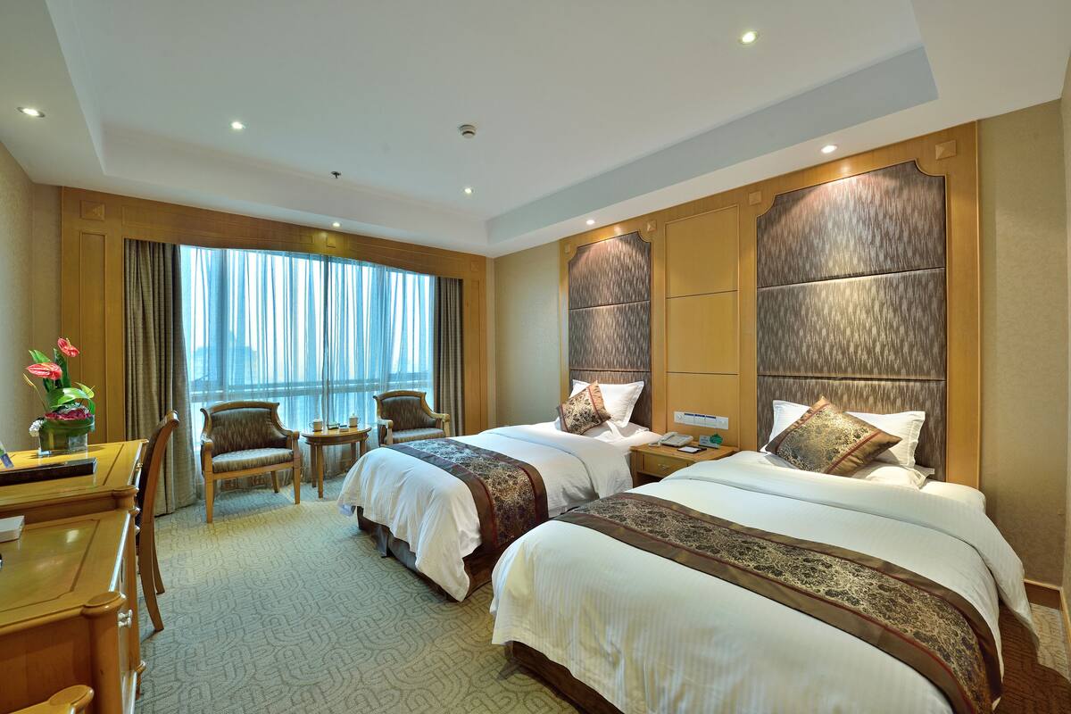 Habitación de hotel con dos camas, un escritorio, una silla y una ventana con cortinas.