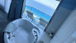 A modern bathroom with a large bathtub, a glass-enclosed balcony with a view of the sea, and a neatly arranged vanity area. - Fener Hotel Cafe & Kahvalti (Cesme)