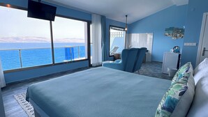 A bedroom with a large bed, a TV, a desk, and a view of the sea. - Fener Hotel Cafe & Kahvalti (Cesme)