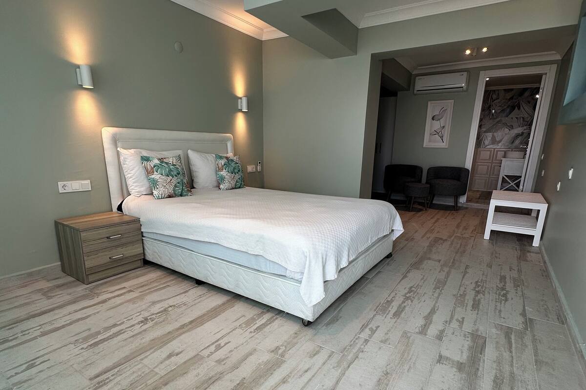 A bedroom with a large bed, wooden flooring, and two wall-mounted lights.
