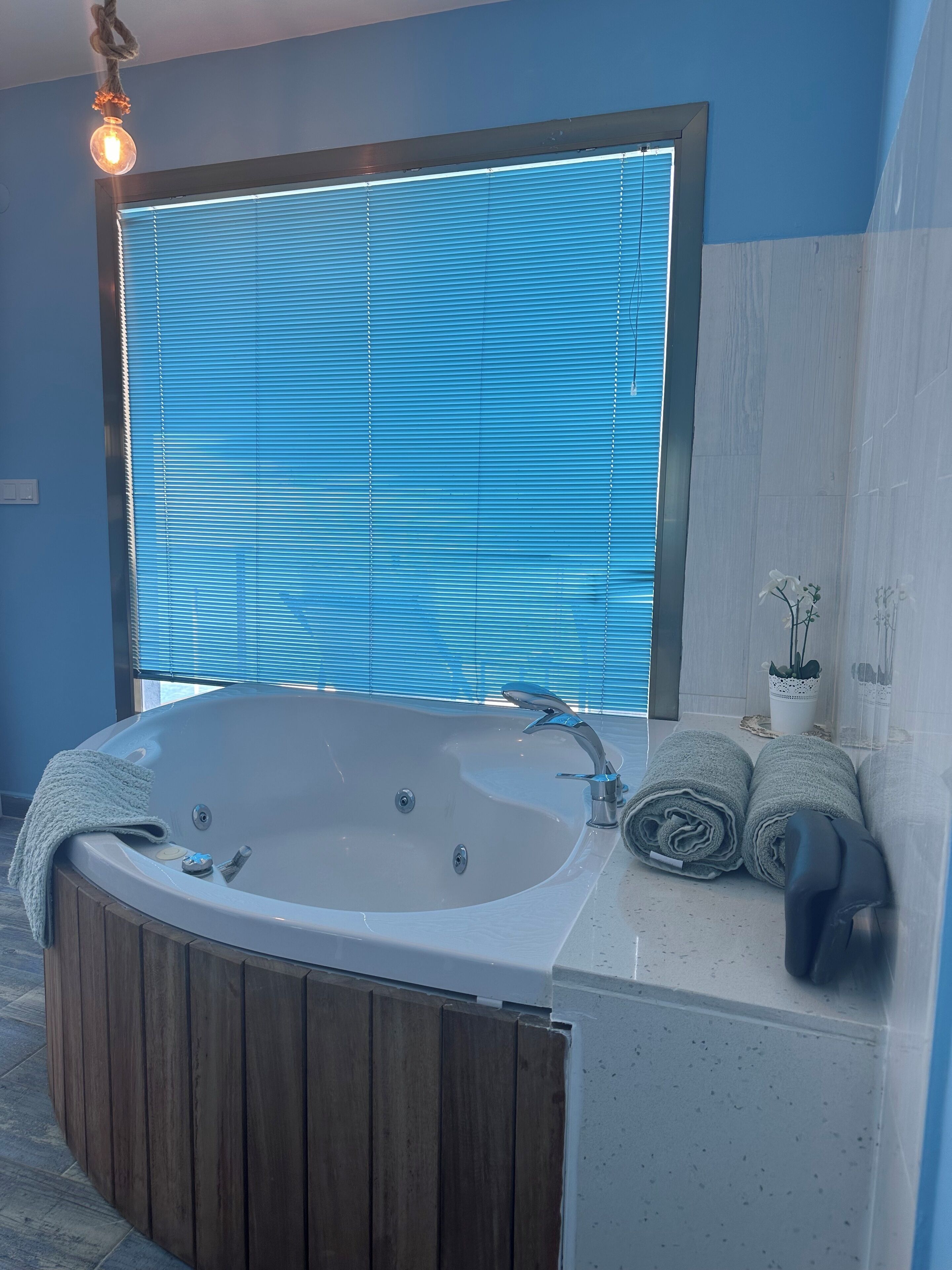 A modern bathroom with a freestanding bathtub, a wooden vanity, and a large window with blinds.