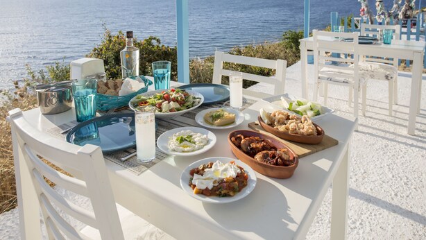 A table set with various dishes and drinks, overlooking a scenic view of the sea and mountains. - Fener Hotel Cafe & Kahvalti (Cesme)