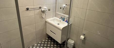 Un baño con lavamanos, espejo y retrete blancos. El piso presenta un estampado de baldosas blanco y negro.