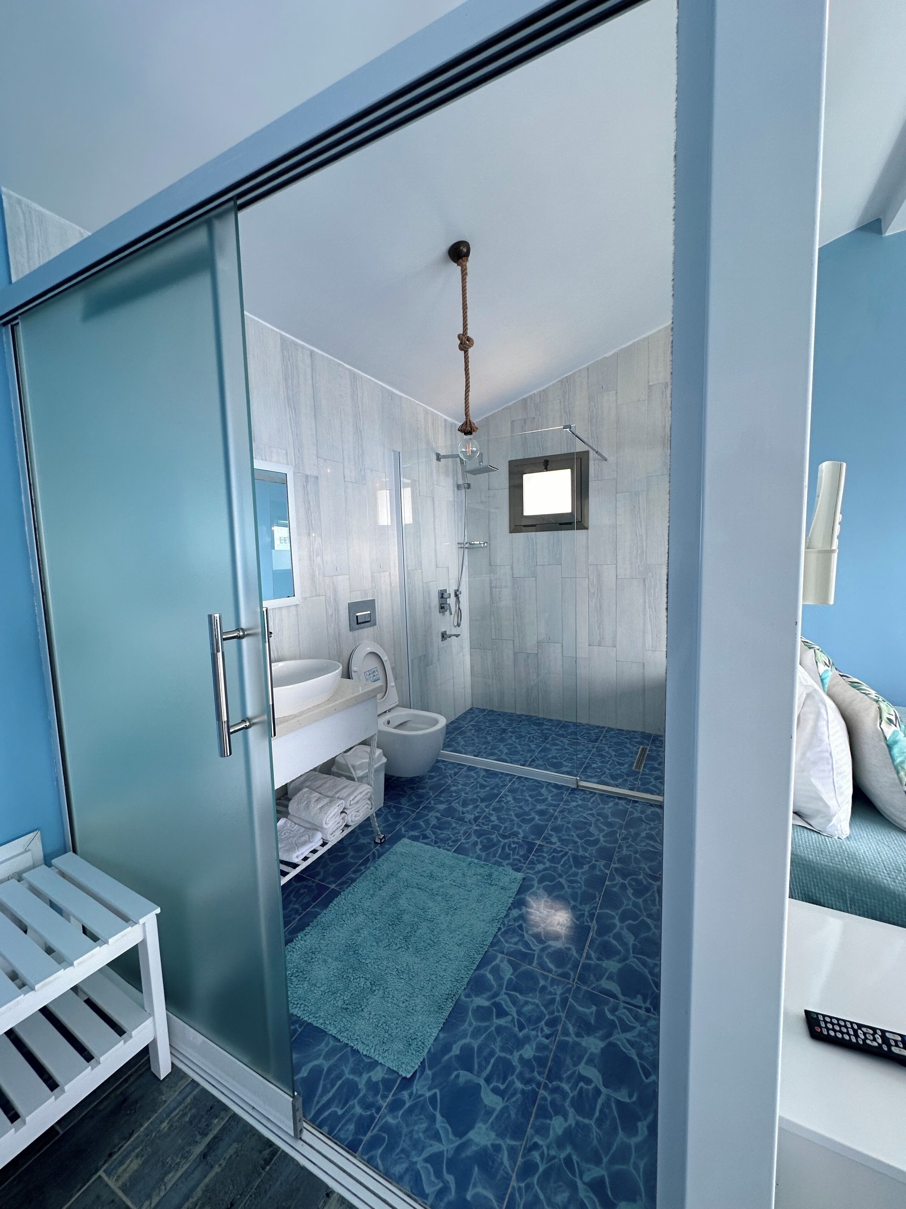 A modern bathroom with a glass shower enclosure, a white sink, and a blue patterned floor.