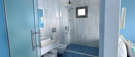 A modern bathroom with a glass shower enclosure, a white sink, and a blue patterned floor.