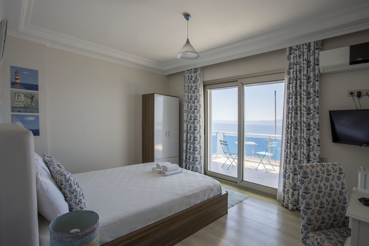 A bedroom with a large bed, a wardrobe, a television, and a balcony with a view of the sea.