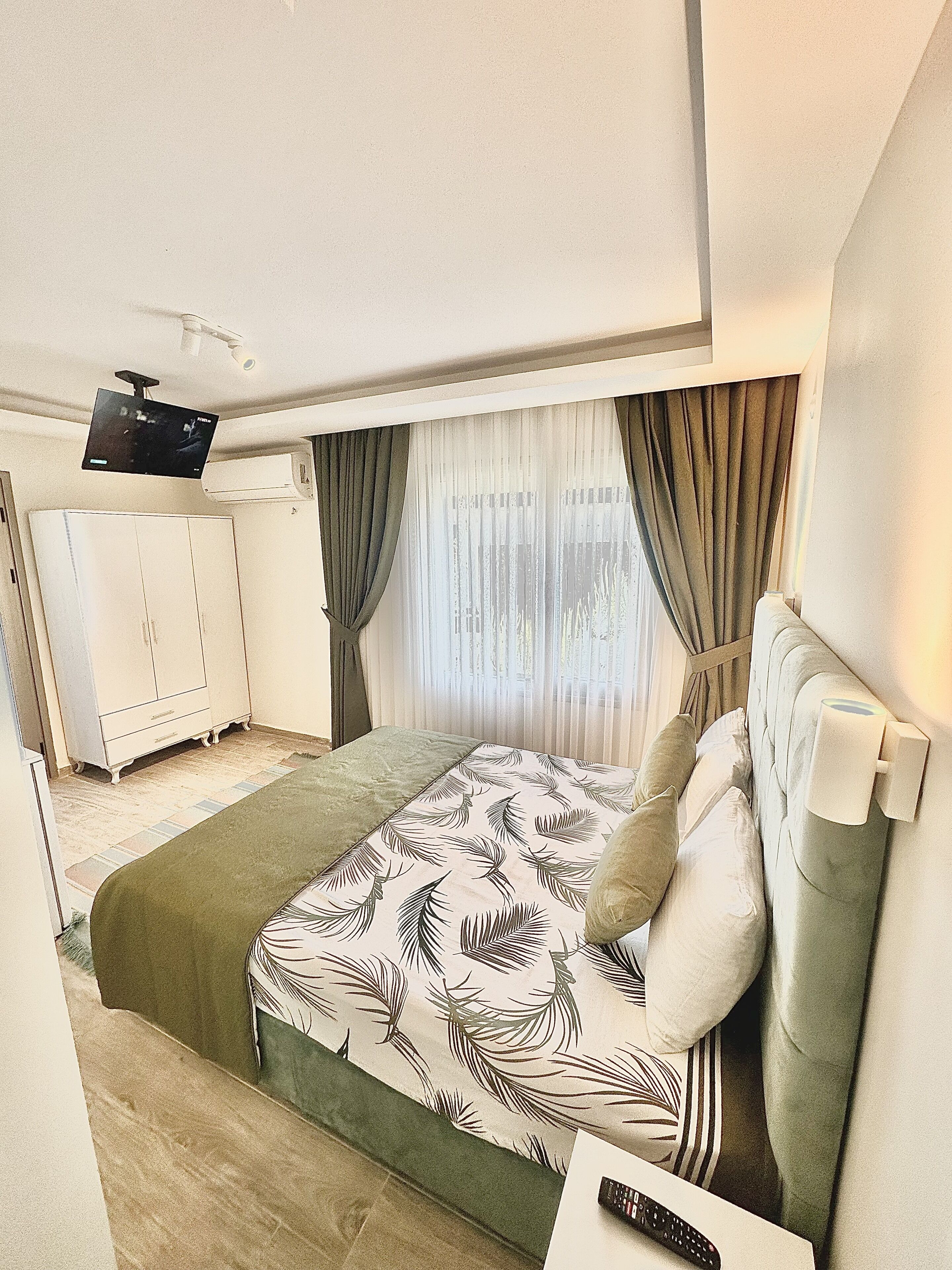 Quarto bem arrumado com uma cama, televisão na parede e um guarda-roupa.