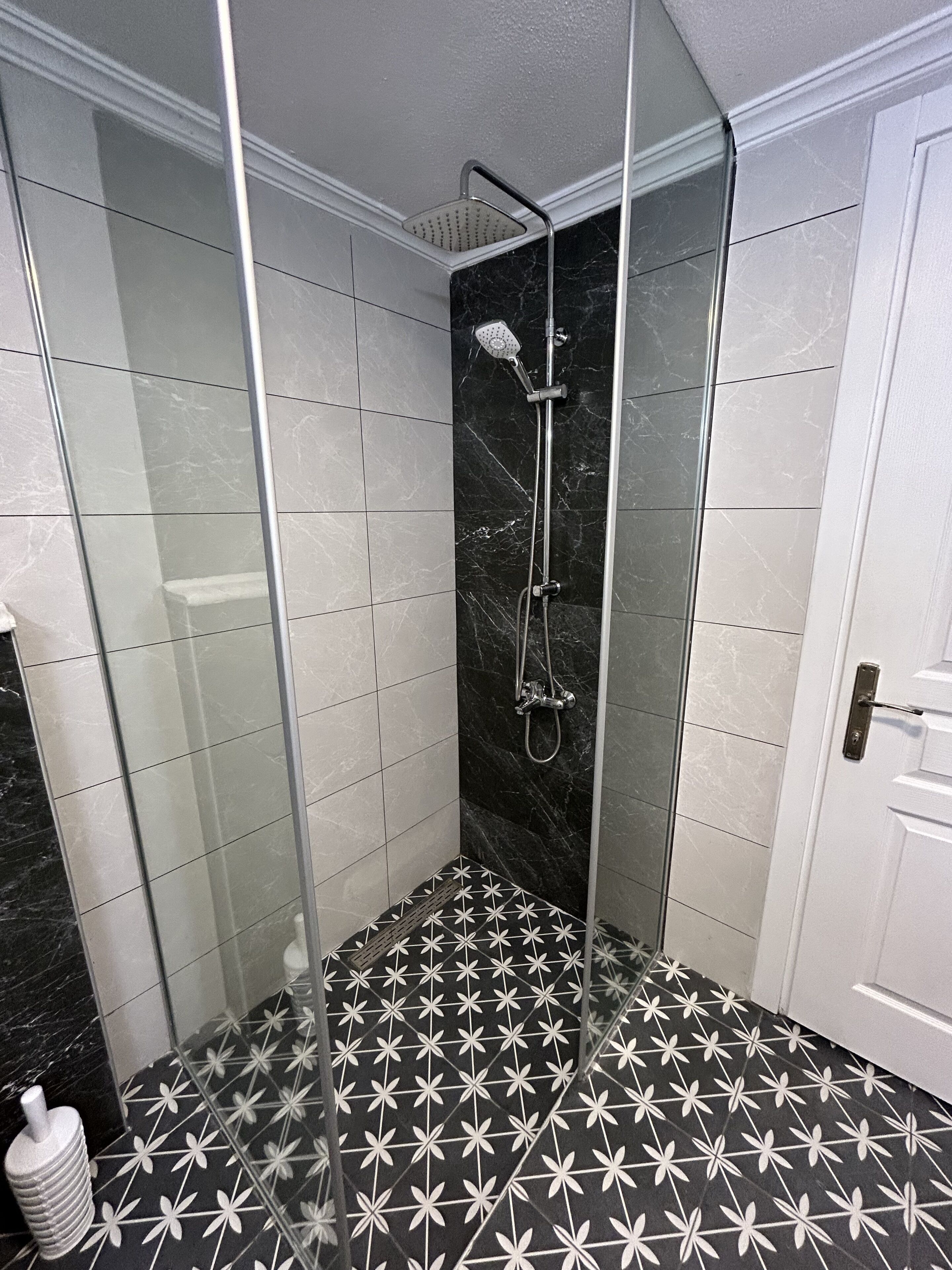 Ein modernes Badezimmer mit einer gläsernen Duschkabine, gefliesten Wänden und einem schwarz-weißen Musterboden.
