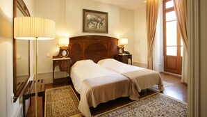 A double room with two beds, a wooden headboard, bedside lamps, a mirror, a painting on the wall, and a window with curtains. - Hotel Ibn-Arrik  (Coimbra)
