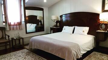 A hotel room with a large bed, a wooden headboard, a mirror, a nightstand, a lamp, and a patterned rug.