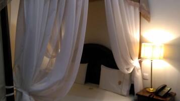 Una camera da letto con un letto a baldacchino, biancheria bianca, una lampada da comodino e un comodino con un telefono.