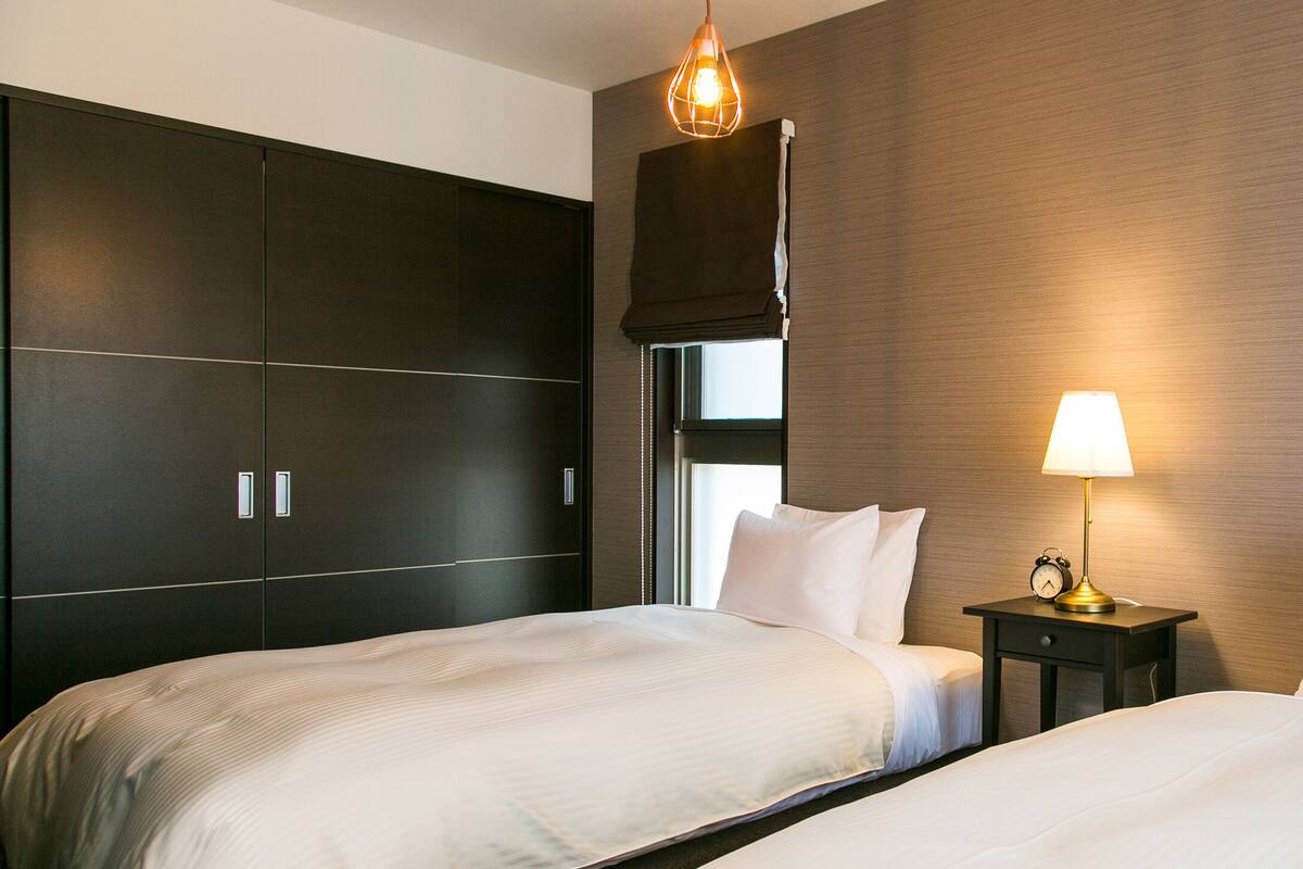 Ein Hotelzimmer mit zwei Betten, einem dunklen Wandschrank, einem Nachttisch mit Lampe und einem Fenster mit Blick.