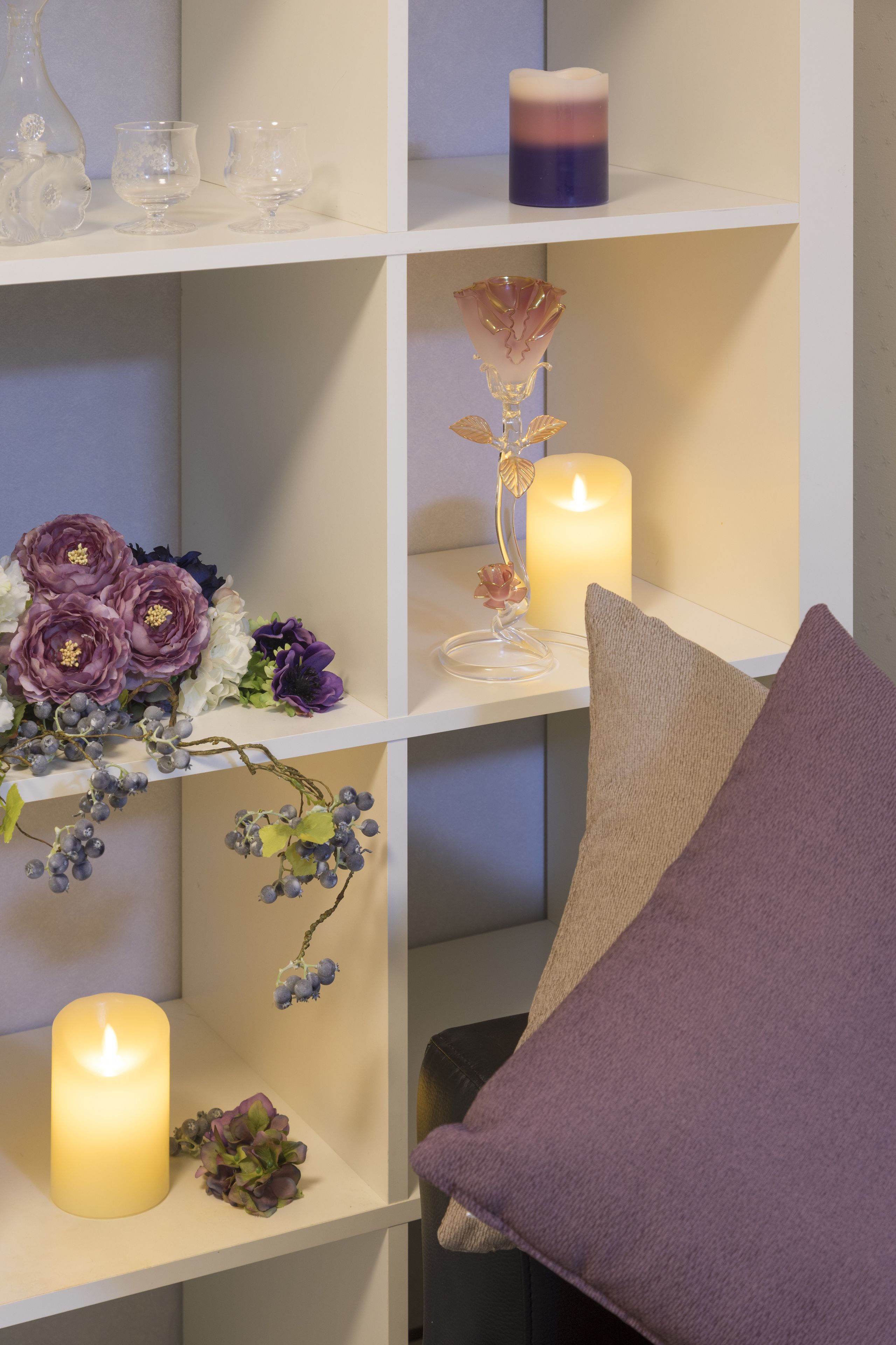 Une étagère avec des bougies, de la verrerie et des fleurs décoratives.
