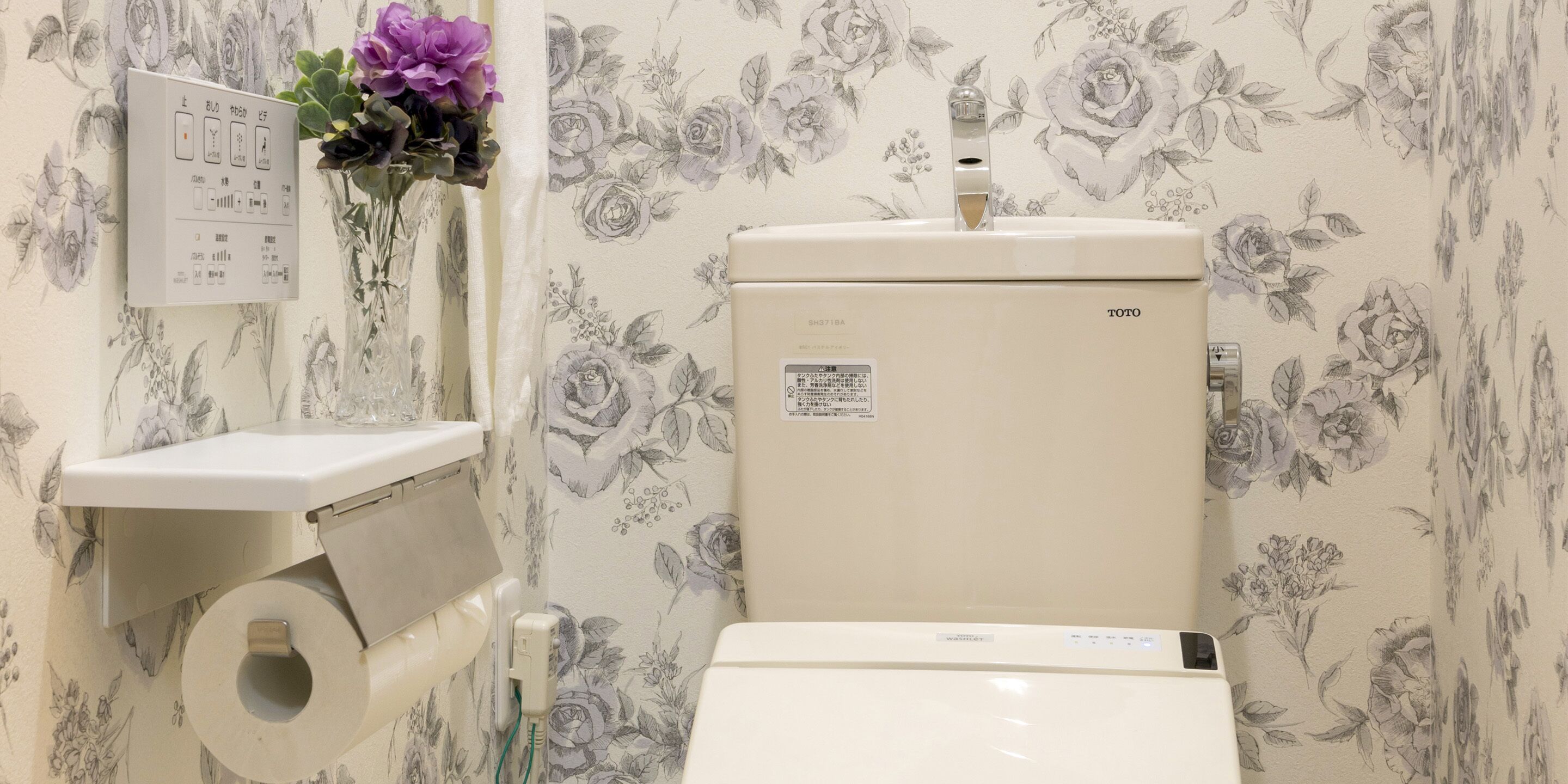 Inodoro con panel de control, dispensador de papel higiénico y papel tapiz floral.