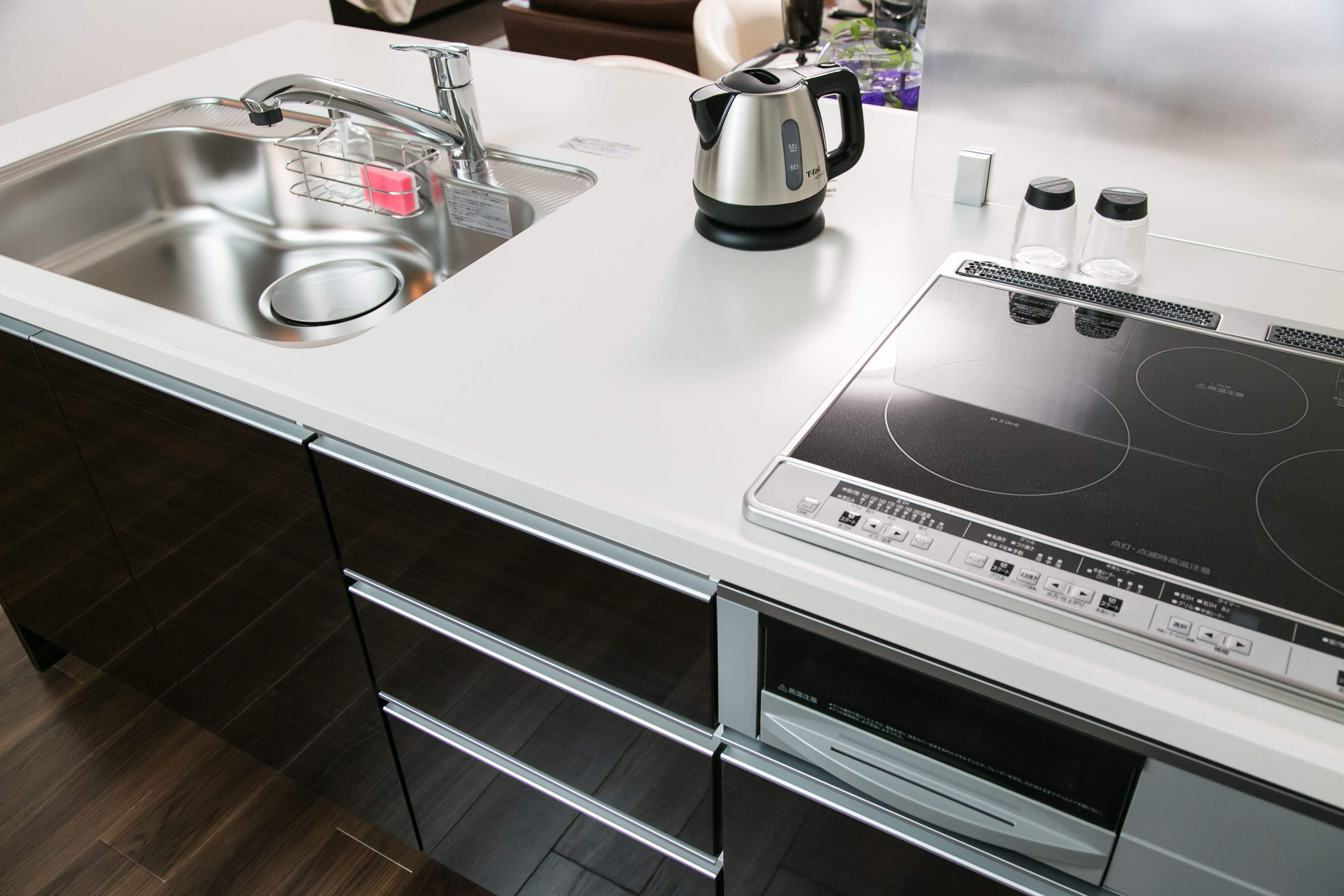 A modern kitchen with a stainless steel sink, a kettle, and a built-in induction cooktop.