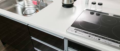 A modern kitchen with a stainless steel sink, a kettle, and a built-in induction cooktop.