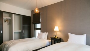 Habitación de hotel con dos camas, un armario, una mesita de noche con lámpara, e iluminación colgante.