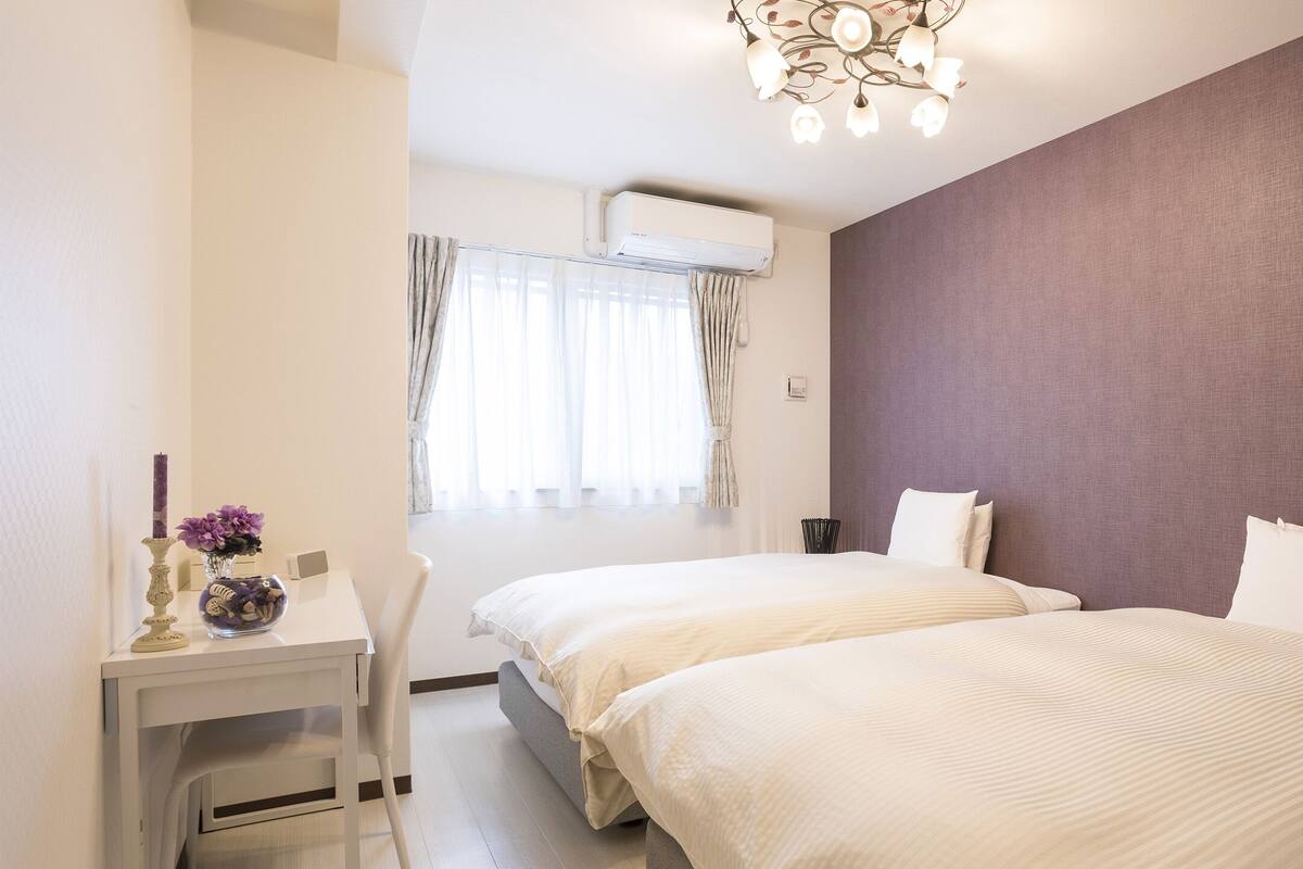 Ein Hotelzimmer mit zwei Betten, einem Schreibtisch, einem Stuhl, einer Vase mit Blumen und einer Deckenleuchte.