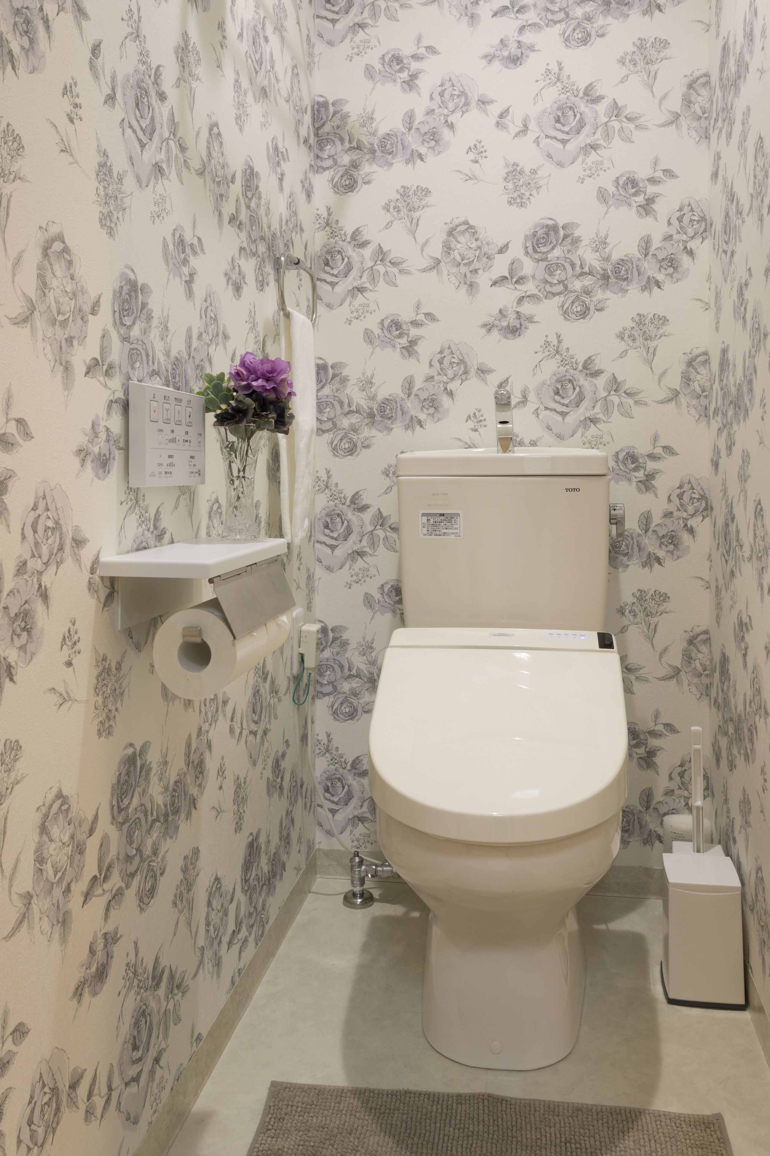 Un bagno con un water, un portasciugamani e un piccolo ripiano con un vaso di fiori.