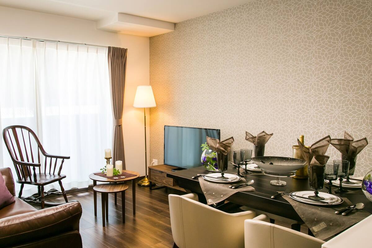 Ein modernes Wohnzimmer mit einem braunen Ledersofa, einem Holzstuhl, einem Esstisch für zwei Personen und einem Fernseher.