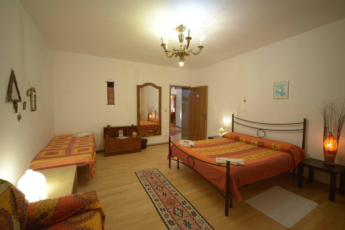 Quarto com duas camas de solteiro, cômoda, espelho, lustre e mesa de cabeceira com abajur.